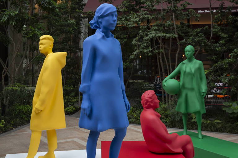 Instalação com quatro esculturas de pessoas, cada uma cobertura de uma cor (amarela, azul, vermelha, verde)