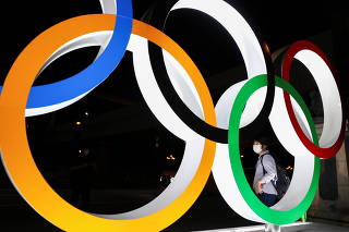 A woman wearing a protective face mask is seen through an illuminated Olympic Rings monument amid the coronavirus disease (COVID-19) pandemic in Tokyo