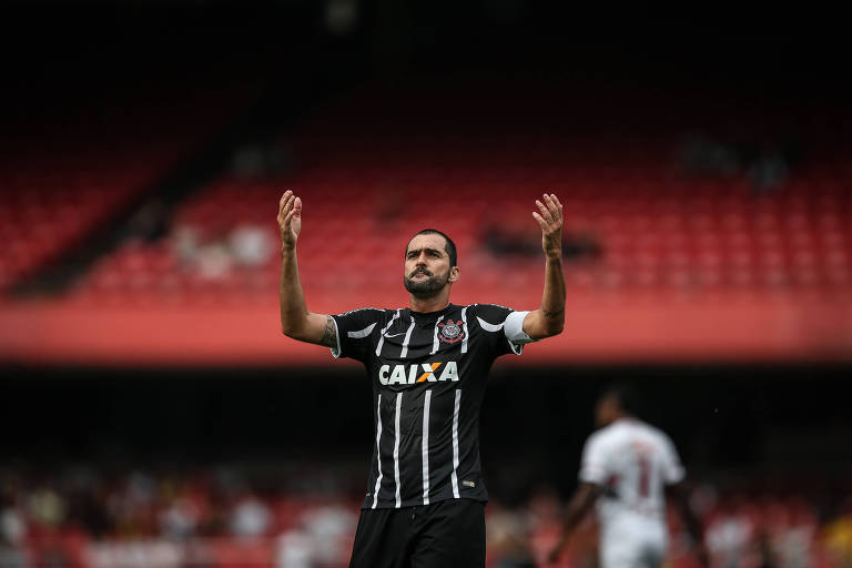 Em destaque, jogador com o uniforme do Corinthians ergue os braços para o alto.