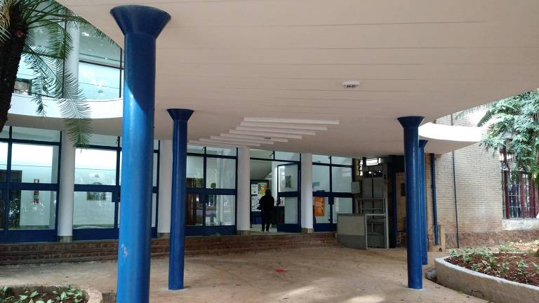 entrada de um predio de vidro com uma cobertura branca e pilastras azuis