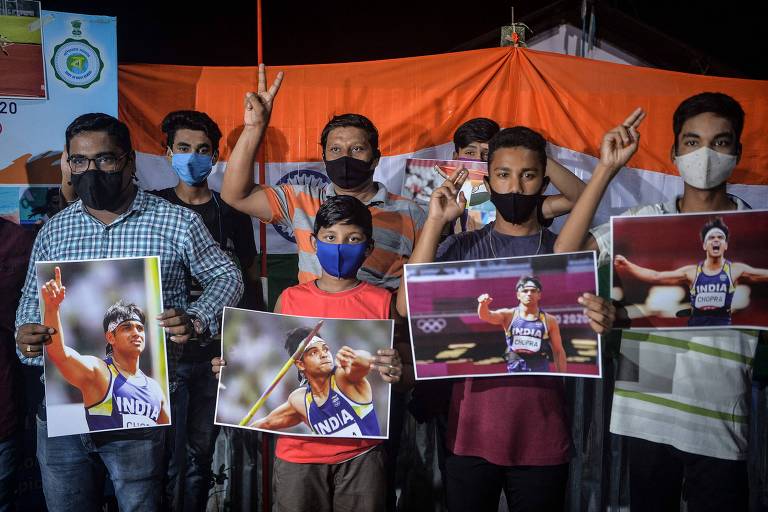 Um grupo de homens posam com cartazes do atleta indiano que ganhou a medalha