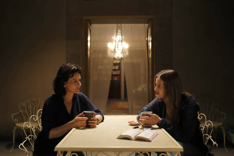 Duas mulheres brancas sentadas frente a frente conversam numa mesa