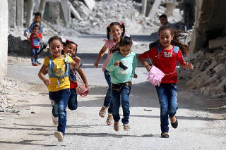 Children run along a damaged street as they celebrate the first day of the Muslim holiday of Eid al-Adha at a rebel-held area in Deraa