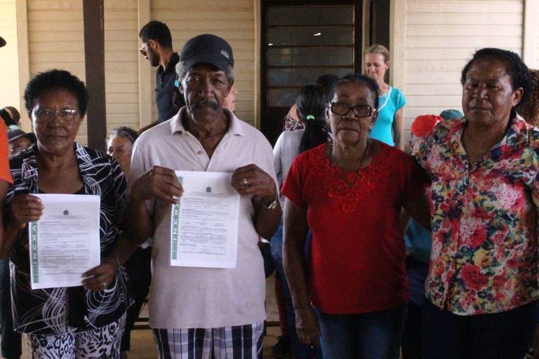 Três mulheres e um homem, todos negros, posam para a foto segurando títulos de propriedade do quilombo