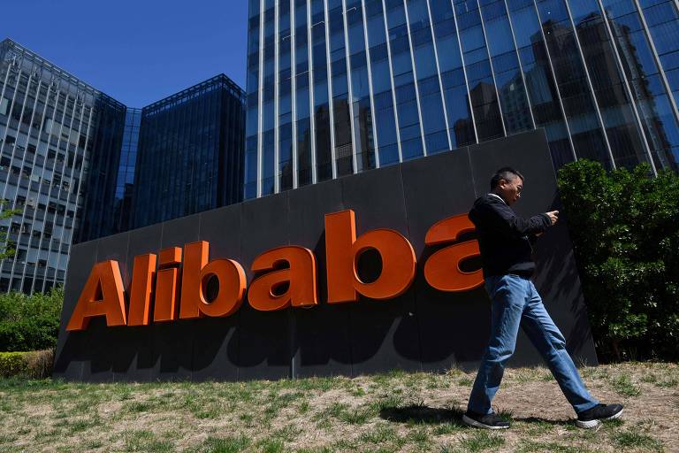 Homem caminha olhando o celular em frente à sede da Alibaba