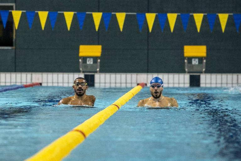 Nadadores lado a lado na piscina abaixo de bandeirolas nas cores azul e amarela