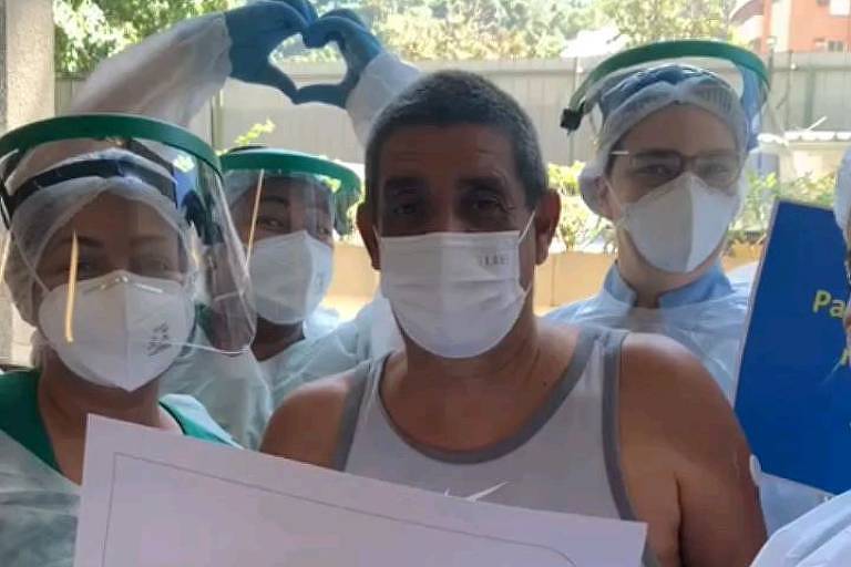 Homem branco de regata branca, usando máscara cirúrgica rodeado de enfermeiros segurando papéis com os dizeres: 'eu venci a Covid-19'