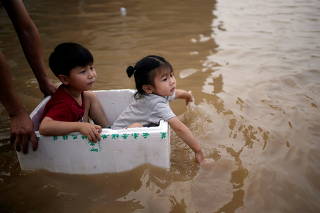 FILE PHOTO: Children sit in a styrofoam container on a flooded road following heavy rainfall in Zhengzhou