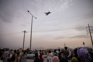 Hoping to flee the country, people gather outside the airport in Kabul, Afghanistan on Friday, Aug. 20, 2021, as a military cargo plane takes off. (Jim Huylebroek/The New York Times)
