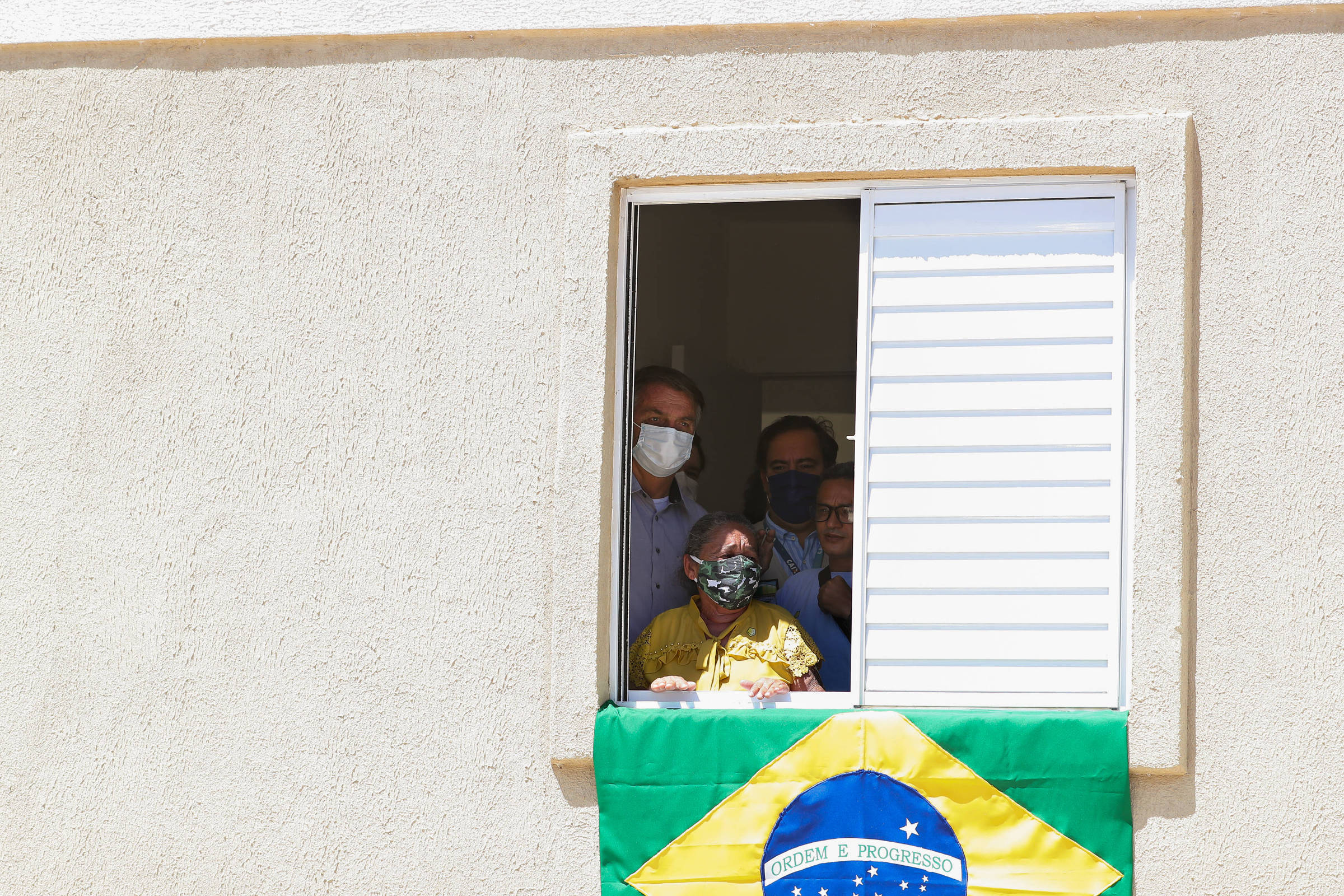 O presidente Bolsonaro, na janela de uma casa, em visita unidade habitacional em Juazeiro do Norte (CE)