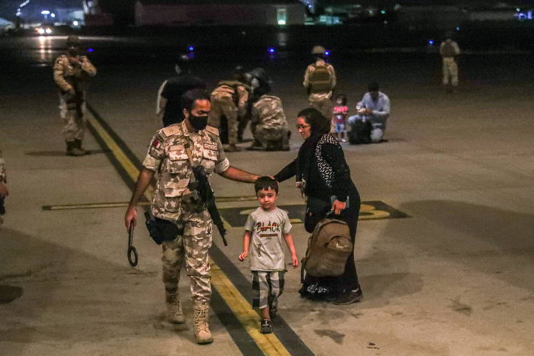 Membro da aeronáutica do Qatar ajuda garoto e mulher resgatados do Afeganistão, na base aérea de Al-Udeid, em Doha