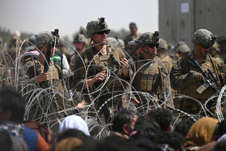 Soldados dos EUA vigiam entrada do setor militar do aeroporto internacional de Cabul, enquanto pessoas tentam acessar o local para sair do país