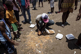A man picks up food from the ground at a food distribution site in Les Cayes, Haiti on Thursday, Aug. 19, 2021. (Adriana Zehbrauskas/The New York Times)