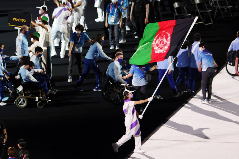 Pessoa vestindo branco carrega a bandeira afegã, nas cores verde, vermelha e preta