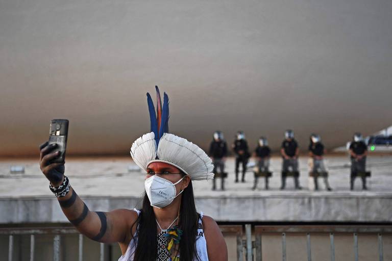 Mulher indígena com cocar de penas tira uma selfie com celular em frente ao prédio do STF