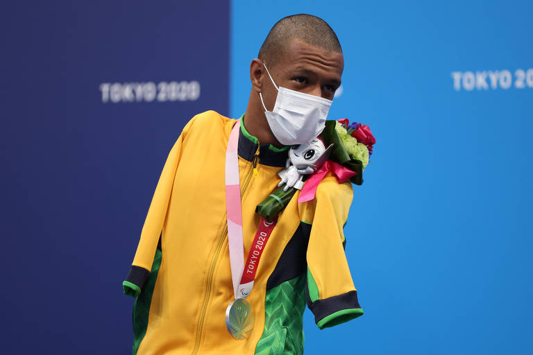 Nadador com agasalho amarelo, máscara e a medalha pendurada no peito