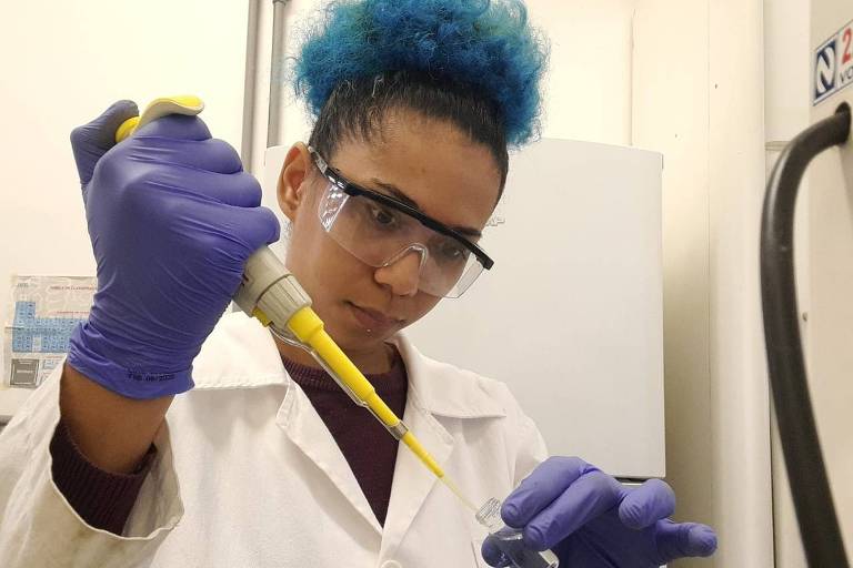 Imagem em primeiro plano mostra uma mulher negra em um laboratório manuseando um experimento.