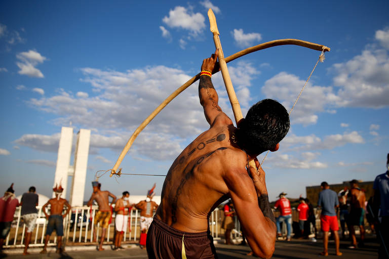 Homem indígena aponta arco e flexa para o prédio do Congresso Nacional