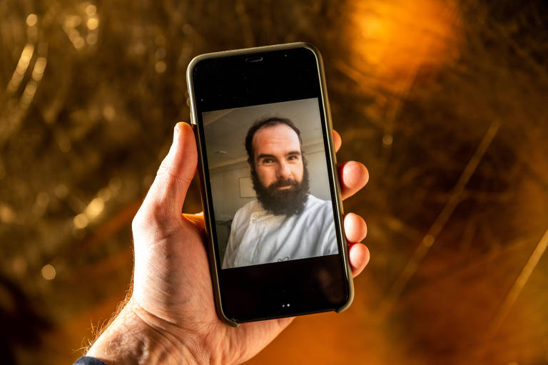 Foto mostra uma tela de telefone celular com a imagem de um homem com barba