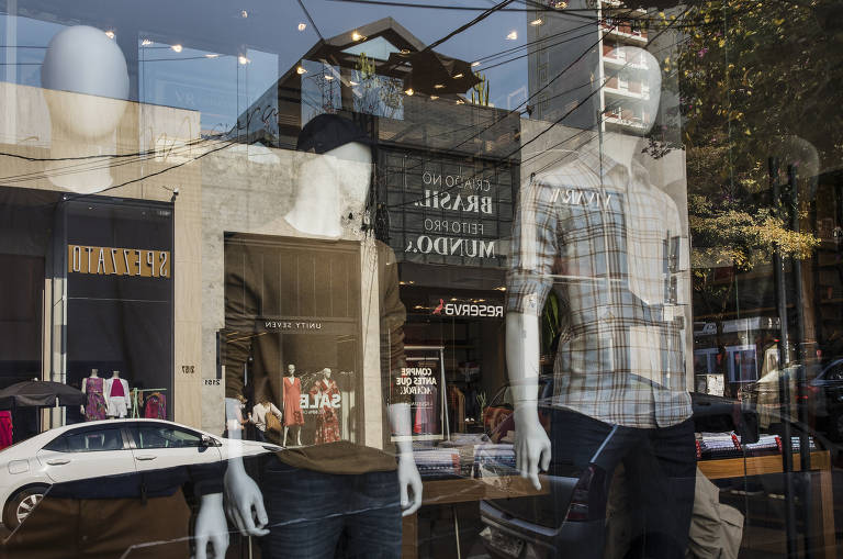 A foto mostra o reflexo da rua Bela Cintra, nos Jardins, em uma vitrine de loja de roupa