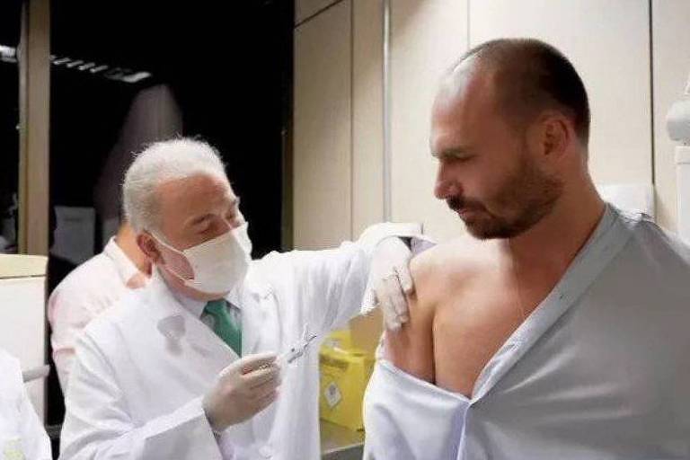 homem de avental aplica vacina no braço de outro homem