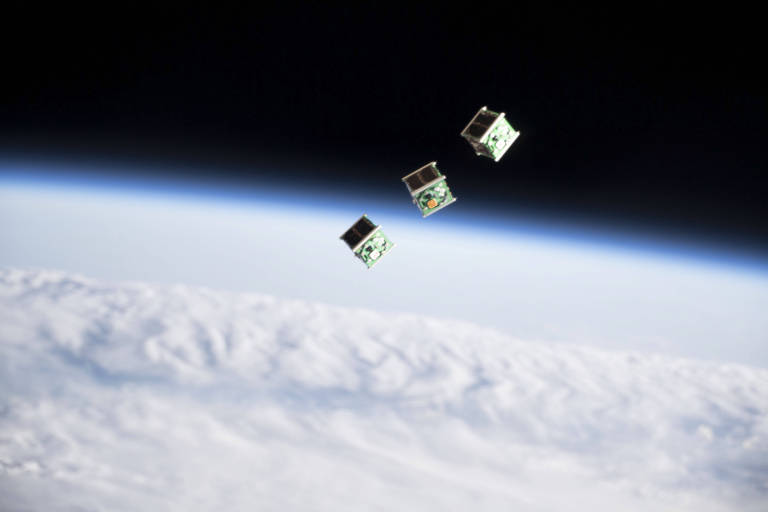 Três pequenos satélites em formato de cubo são vistos na órbita da terra