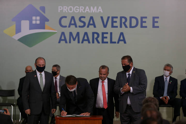Imagem mostra Bolsonaro, rodeado de ministros e políticos, enquanto assina um documento. Atrás deles, há um telão com os dizeres "Casa Verde e Amarela"