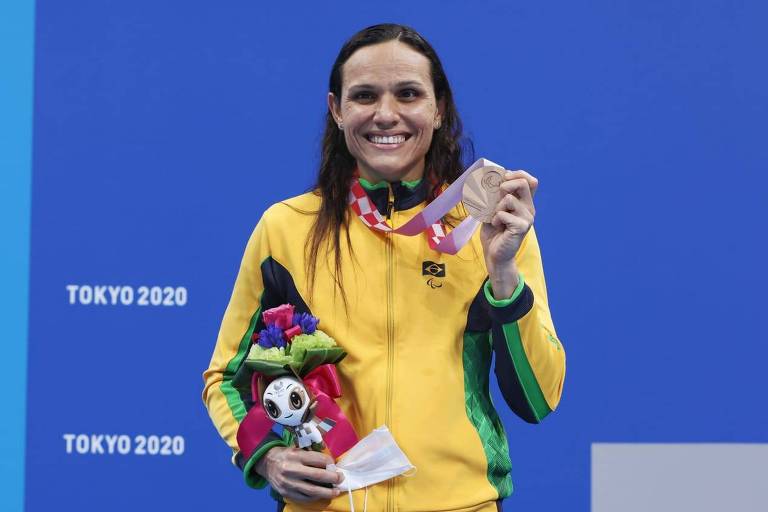 Carol Santiago, de agasalho amarelo, sorri e mostra medalha de bronze