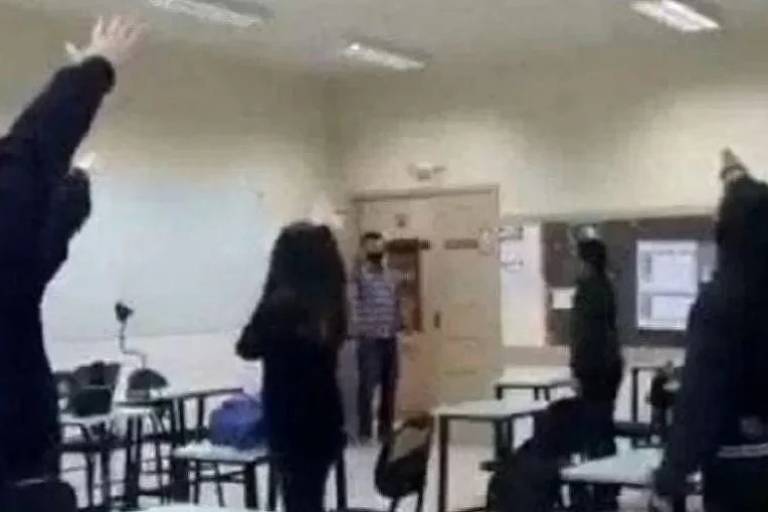 Alunos aparecem de costas, em pé, em sala de aula fazendo saudação nazista