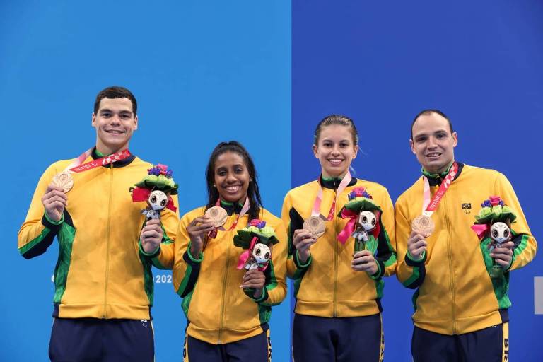 Quatro nadadores lado a lado com agasalho amarelo e mostrando suas medalhas