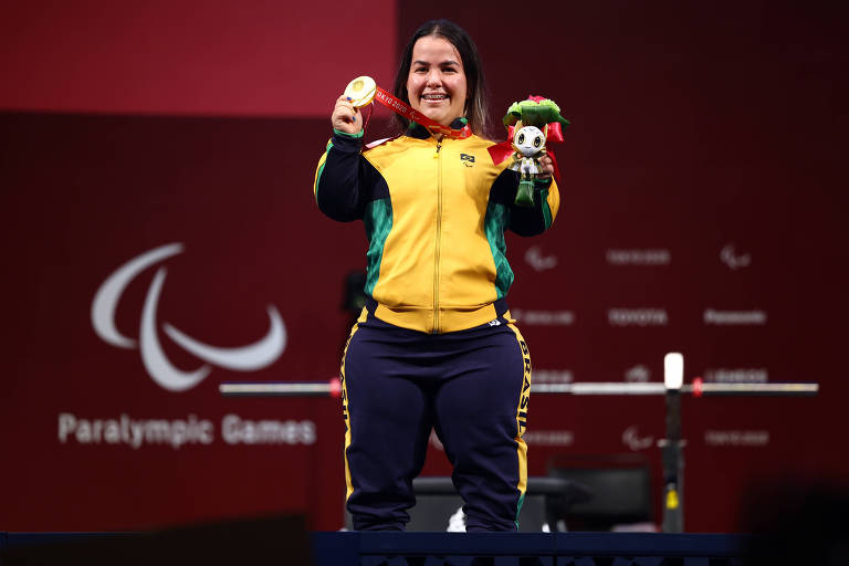 Mariana mostra a medalha de ouro e sorri em frente ao peso