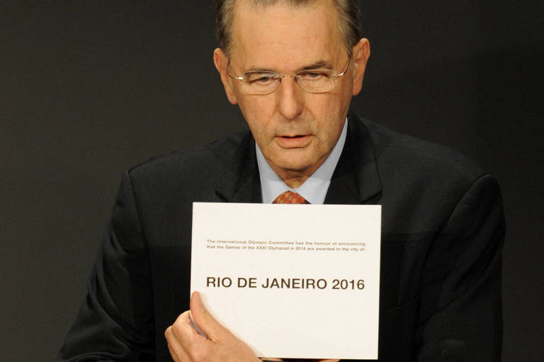 Jacques Rogge durante anúncio do Rio de Janeiro como sede das Olimpíadas de 2016. ele segura uma placa com o nome da cidade brasileira
