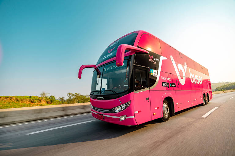 Ônibus cor de rosa da Buser em estrada.