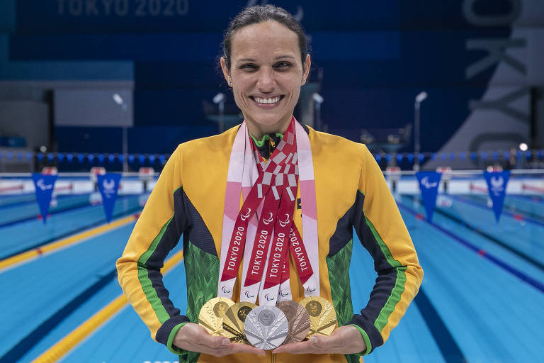 Carol em frente à piscina com cinco medalhas penduradas no pescoço