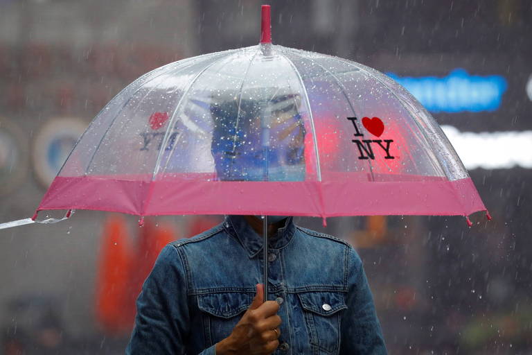 Homem, com máscara e guarda-chuva, protege-se de chuva na Times Square, em Nova York