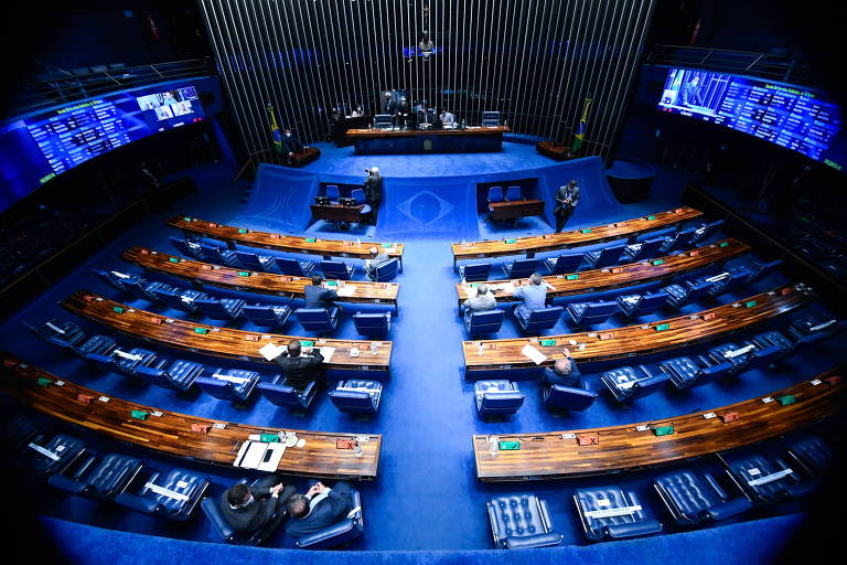 Foto feita do alto mostra o Senado, com bancadas de madeira e cadeira e piso azul; há poucas pessoas na sala
