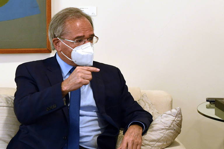 O ministro Paulo Guedes sentado em sofá, de máscara