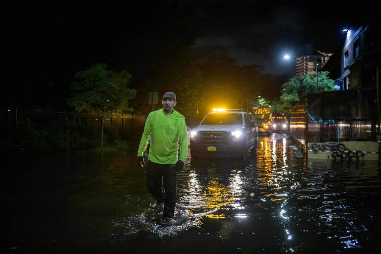 Funcionário da coleta de lixo verifica profundidade de rua inundada no bairro do Brooklyn, em Nova York