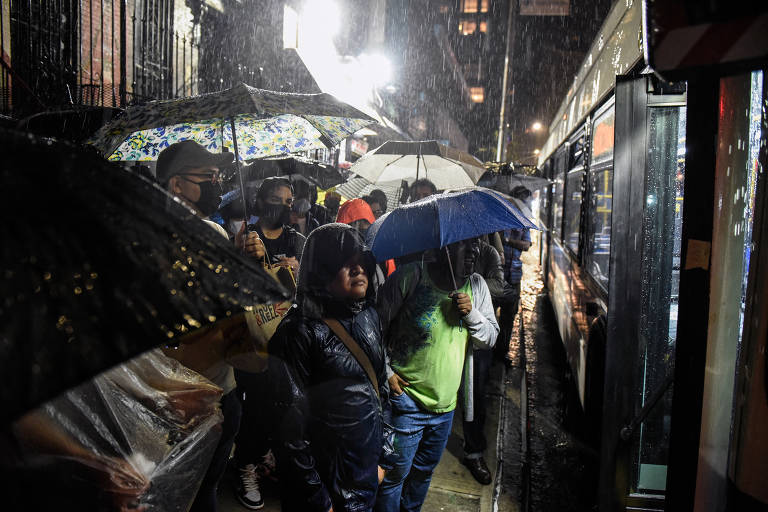 Passageiros esperam sob as fortes chuvas em um ponto de ônibus no Brooklyn, em Nova York, tentando fugir da tempestade