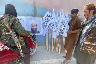 Taliban members stand near a poster of their leader Mullah Haibatullah Akhundzada, in Kabul