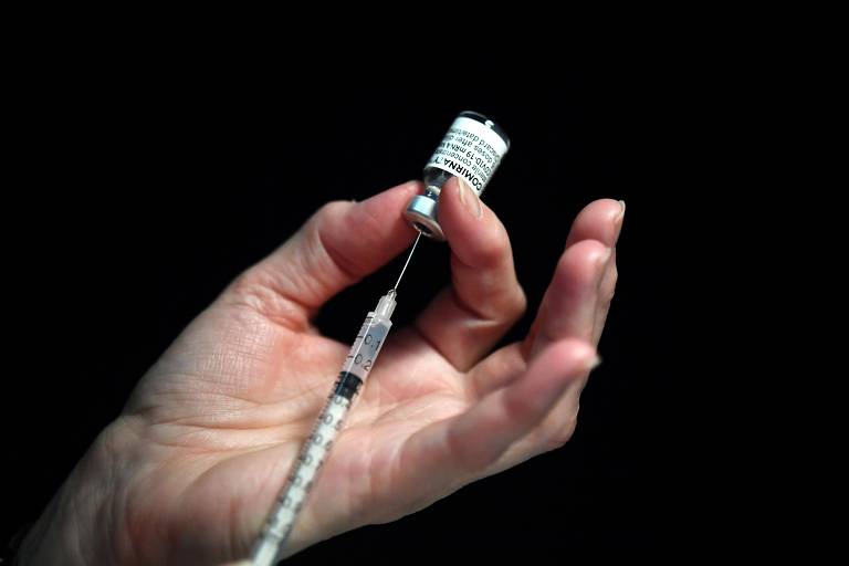 Mãos de uma enfermeira seguram frasco de vacina e uma seringa