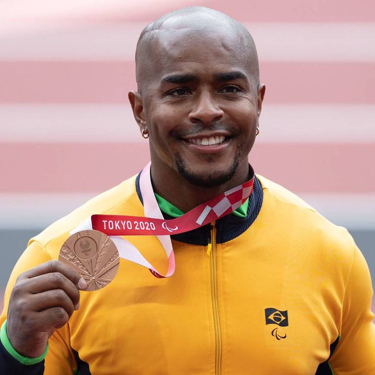 João Victor, de agasalho amarelo, sorri e segura a medalha de bronze com a mão direita