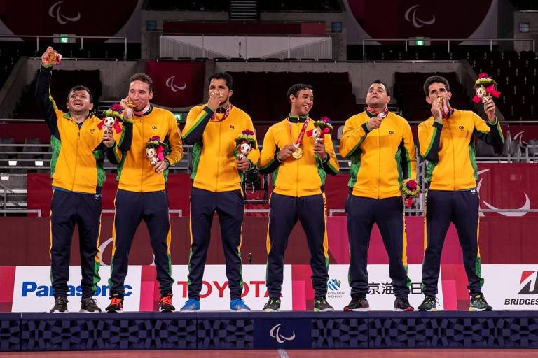 Atletas brasileiros perfilados no pódio com agasalhos amarelos