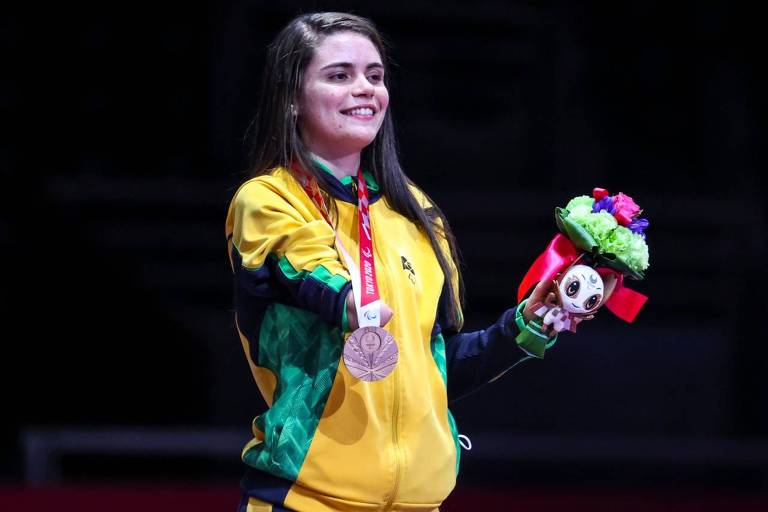 Silvana Fernandes com agasalho amarelo, medalha no peito e sorrindo em foto com fundo escuro