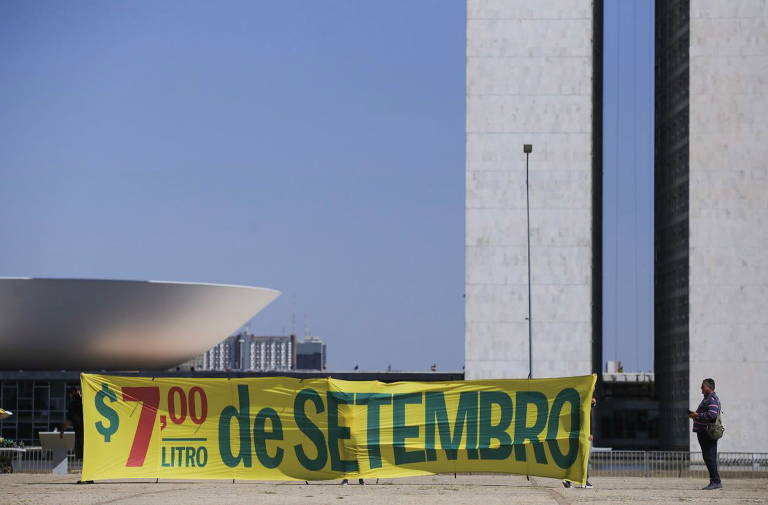 Faixa amarela com os dizeres "$7,00/litro de Setembro" é vista em frente ao Congresso Nacional. As letras estão em verde e os números em vermelho
