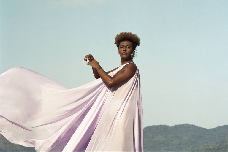 Mulher trans negra com um vestido lilás sendo movido pelo vento