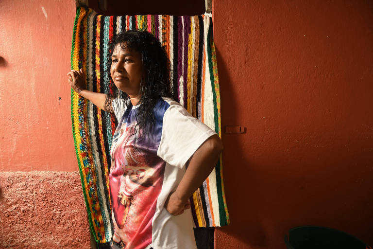 A ajudante de salão de beleza Marinalva Ferraz, que não consegue trabalho fixo, de pé, encostada em uma cortina colorida de sua casa 