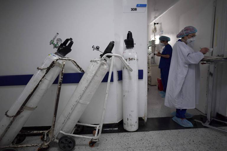 Três cilindros brancos de oxigênio estão apoiados em um corredor branco de hospital
