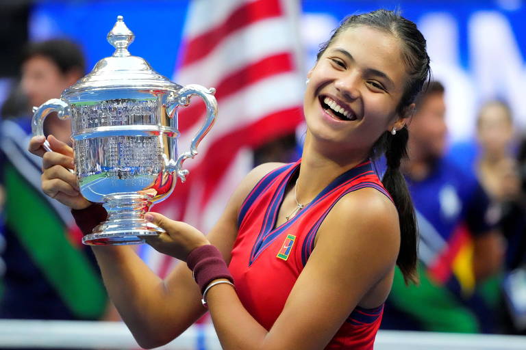 Tenista vestida com roupa vermelha sorri segurando o troféu