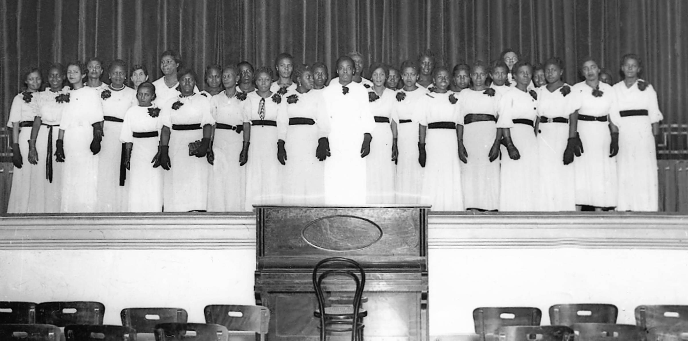Imagem em preto e branco mostra um grupo de mulheres em um palco